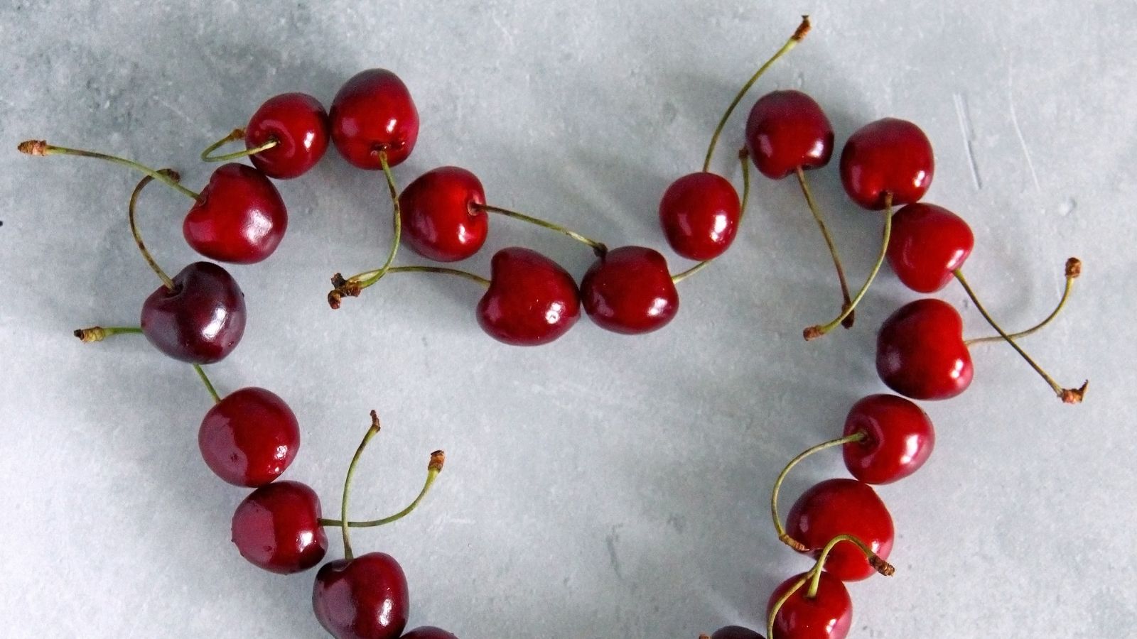 Cerezas formando un corazon sobre superficie clara, imagen editorial sobre salud cardiometabolica.
