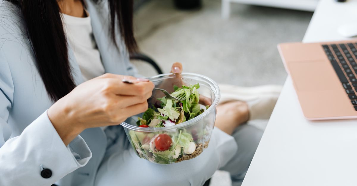 Adult woman eating a vegetable salad at her office desk, embodying healthy lunchtime habits.