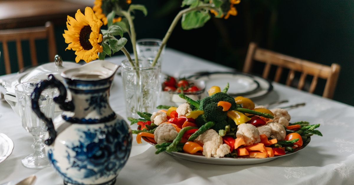 A beautifully set dining table with fresh vegetables, sunflowers, and an ornate jug creates a cozy atmosphere.
