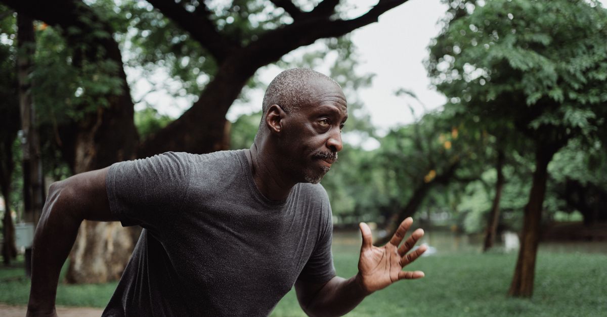 Focused black male adult running energetically in a green park, promoting fitness and health.