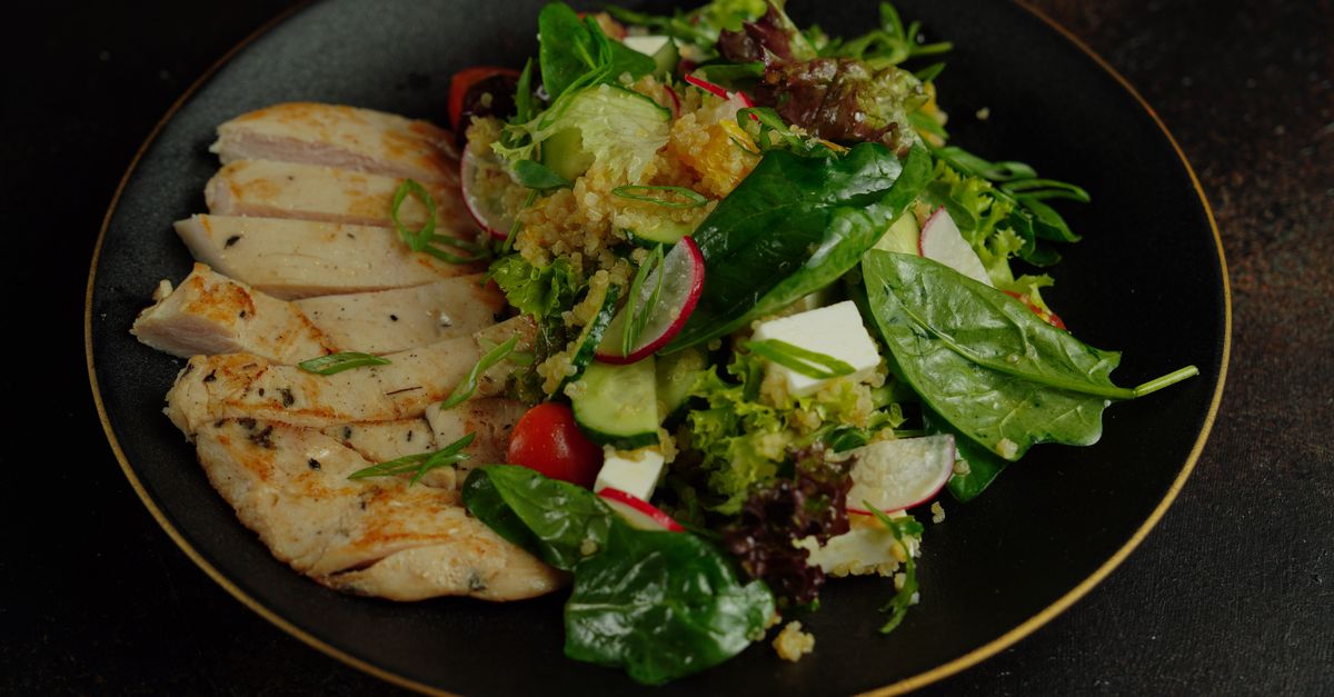 A vibrant salad featuring grilled chicken, quinoa, and fresh vegetables on a black plate.