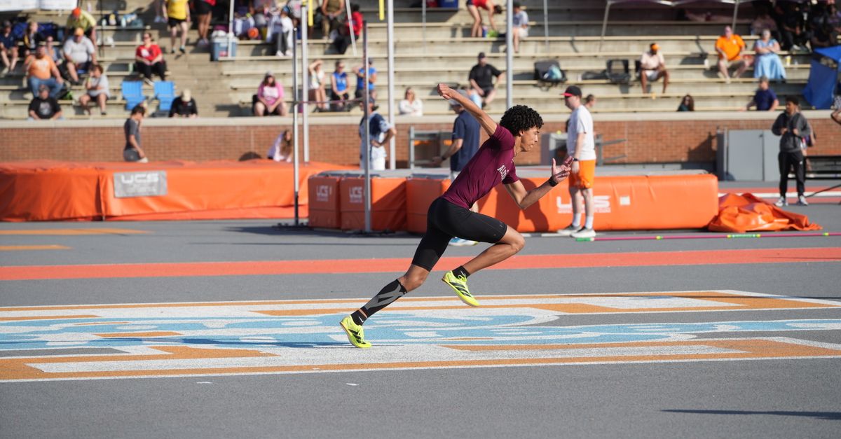 Athlete sprinting on track during a sunny outdoor sports meet.