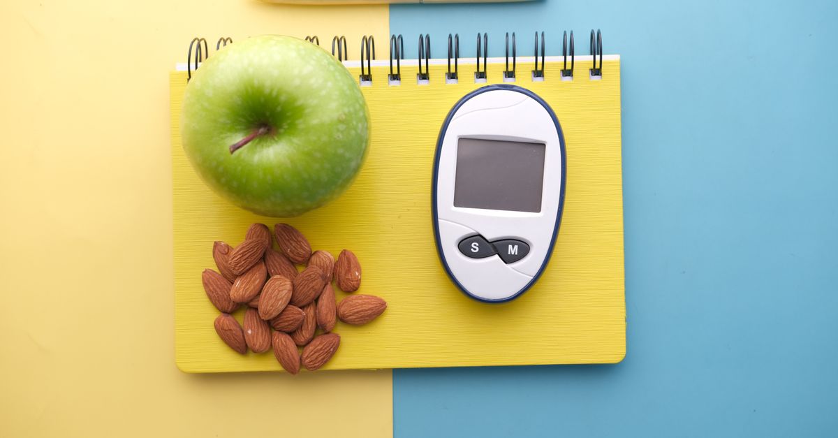 Flat lay of diabetes tools, green apple, almonds, and notebook for health planning.