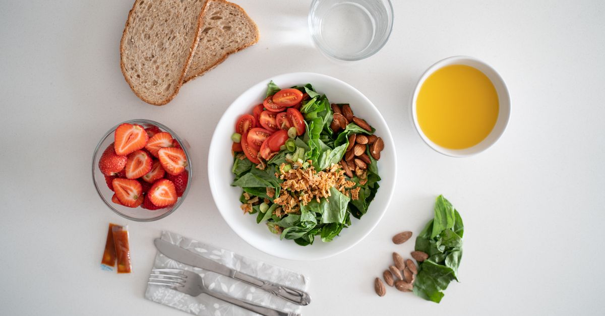 Top view of a healthy salad and fresh ingredients with bread and juice on a white surface.