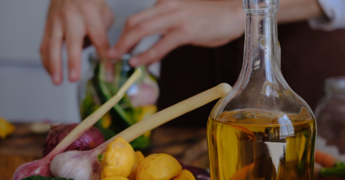 Hands preparing vegetables with olive oil, garlic, and squash in a kitchen setting.
