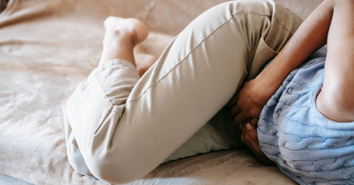 Crop anonymous barefoot female in casual outfit lying on couch while having acute stomach ache