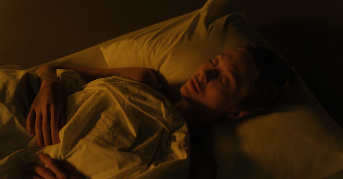 A woman peacefully sleeping in a dimly lit bedroom, wrapped in a white blanket.
