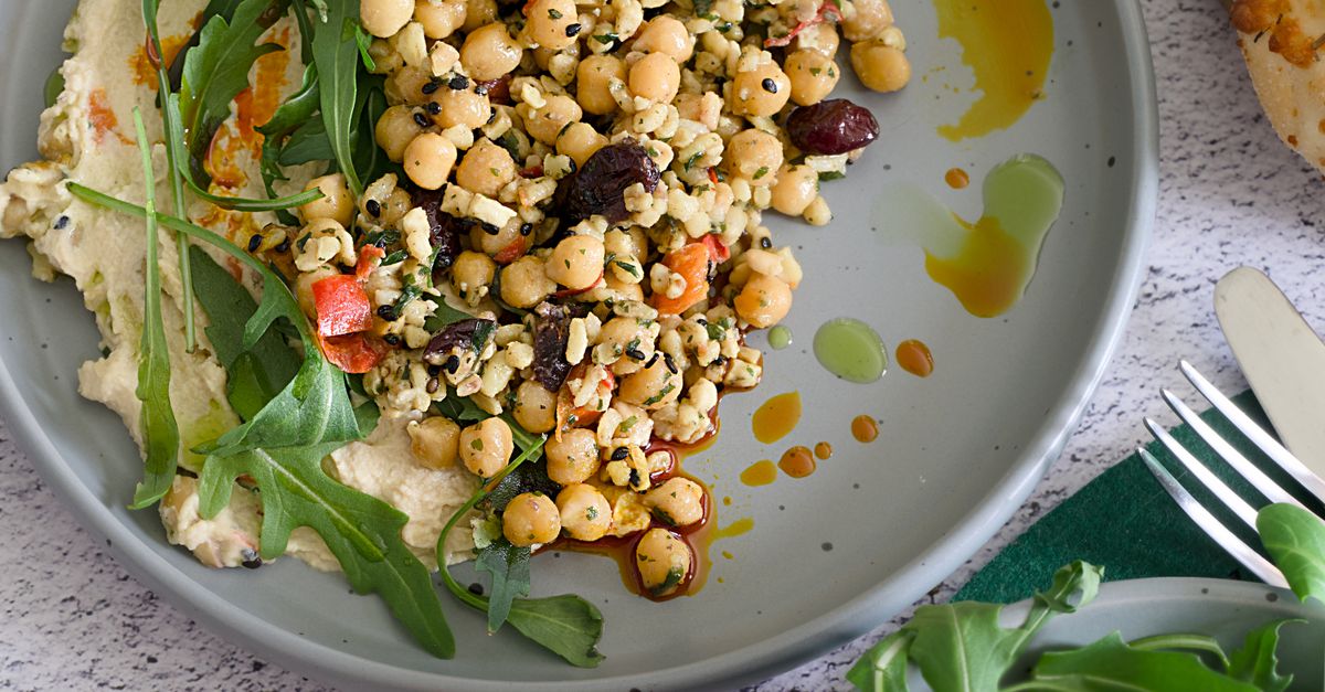 Delicious Mediterranean salad with chickpeas, hummus, arugula, and olives, drizzled with olive oil.