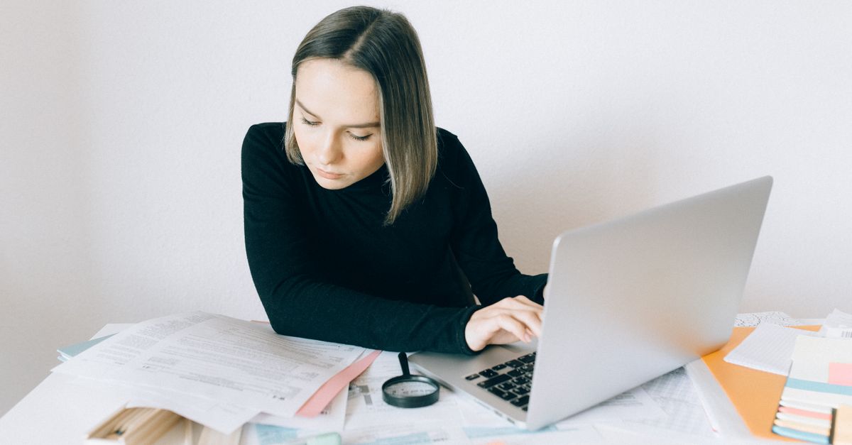 Focused woman researching on a laptop, surrounded by paperwork in a modern office.