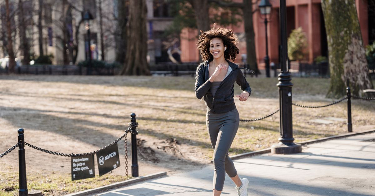 Full body of African American female jogger in sportswear smiling and running in park