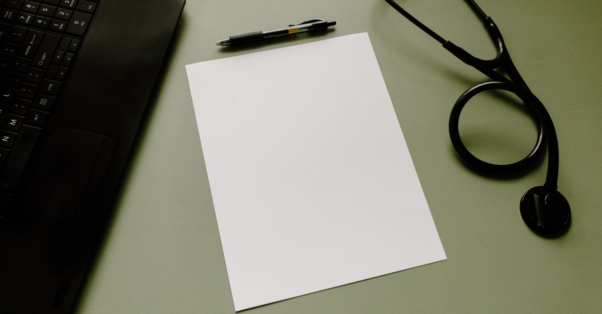 Professional workspace featuring a laptop, stethoscope, pen, and paper sheet for healthcare tasks.