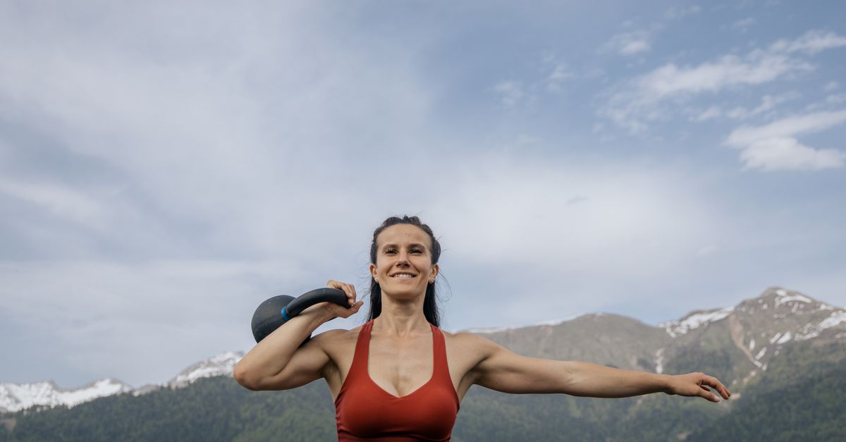A fit woman in sportswear exercises with a kettlebell in a scenic mountain landscape.