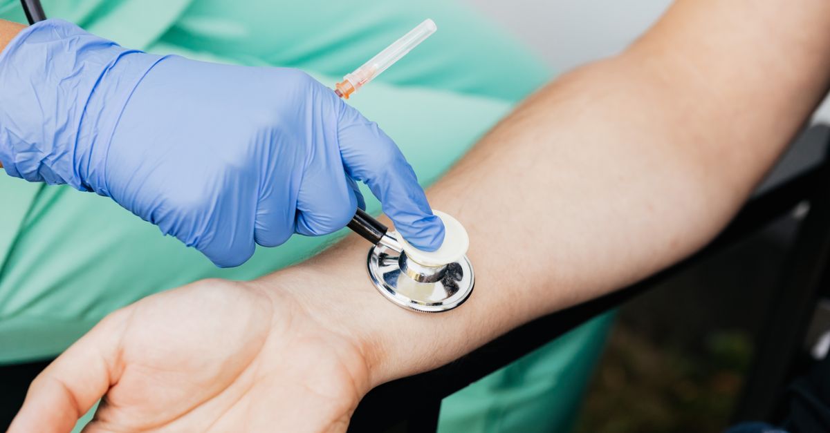 Healthcare professional using a stethoscope on patient's wrist during a medical exam.