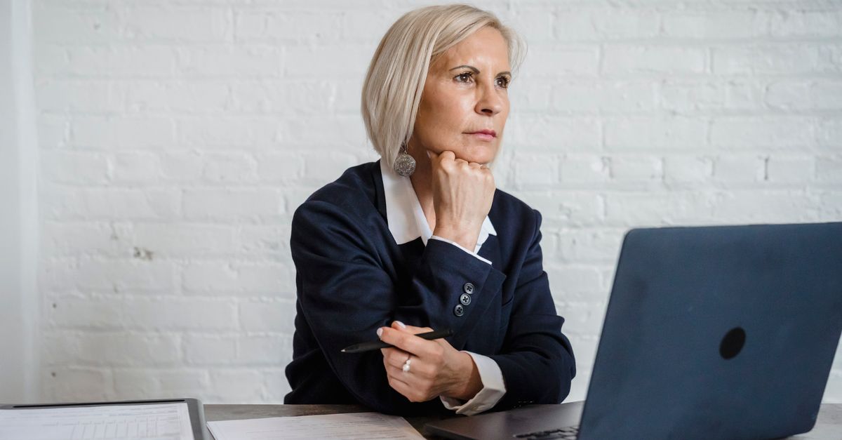 Professional woman in deep thought, working on a laptop indoors, suggesting mental focus and business acumen.