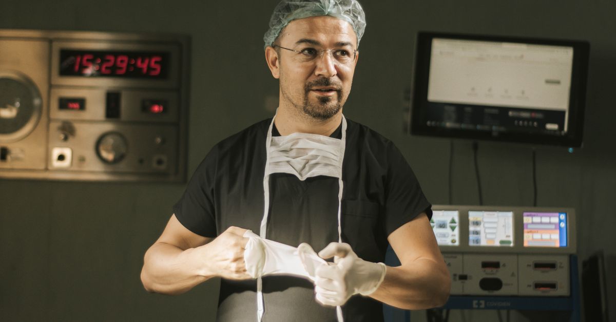 A male surgeon in scrubs and mask prepares for surgery in a hospital operating room.