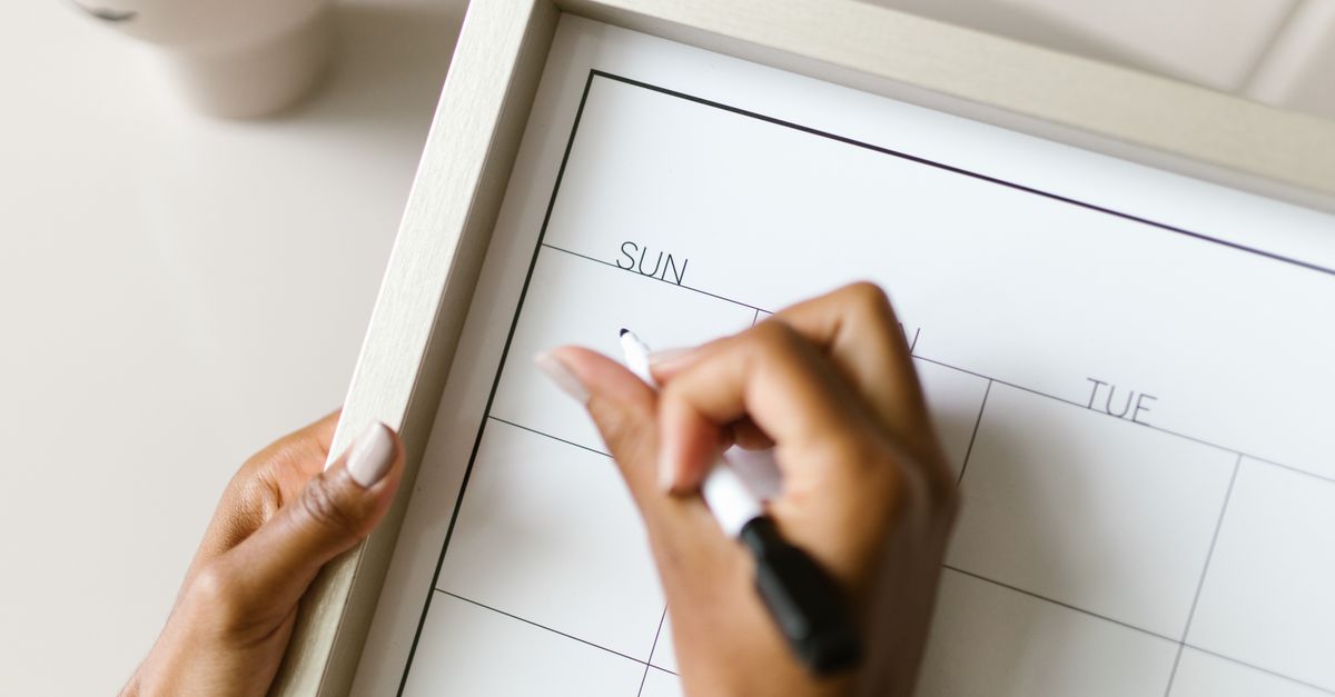 Hands holding a wall calendar, writing with a marker, organizing schedule.