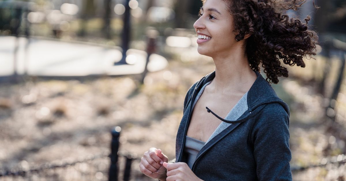 Side view of young African American female smiling while running in park against blurred background