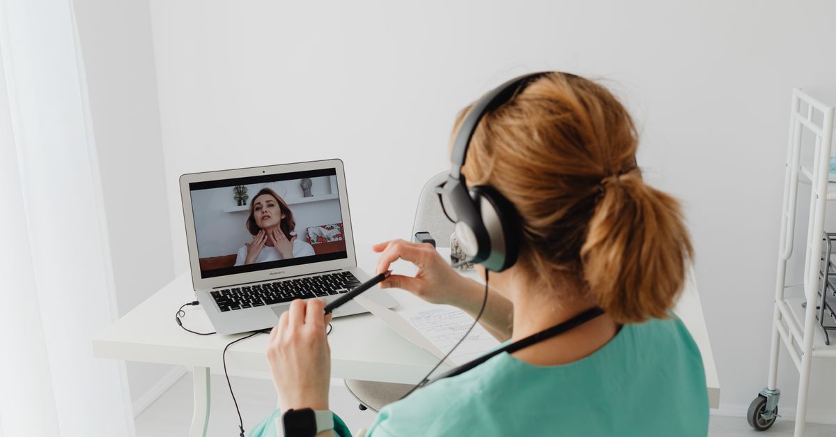 A doctor conducting an online consultation with a patient via laptop in a modern office setting.