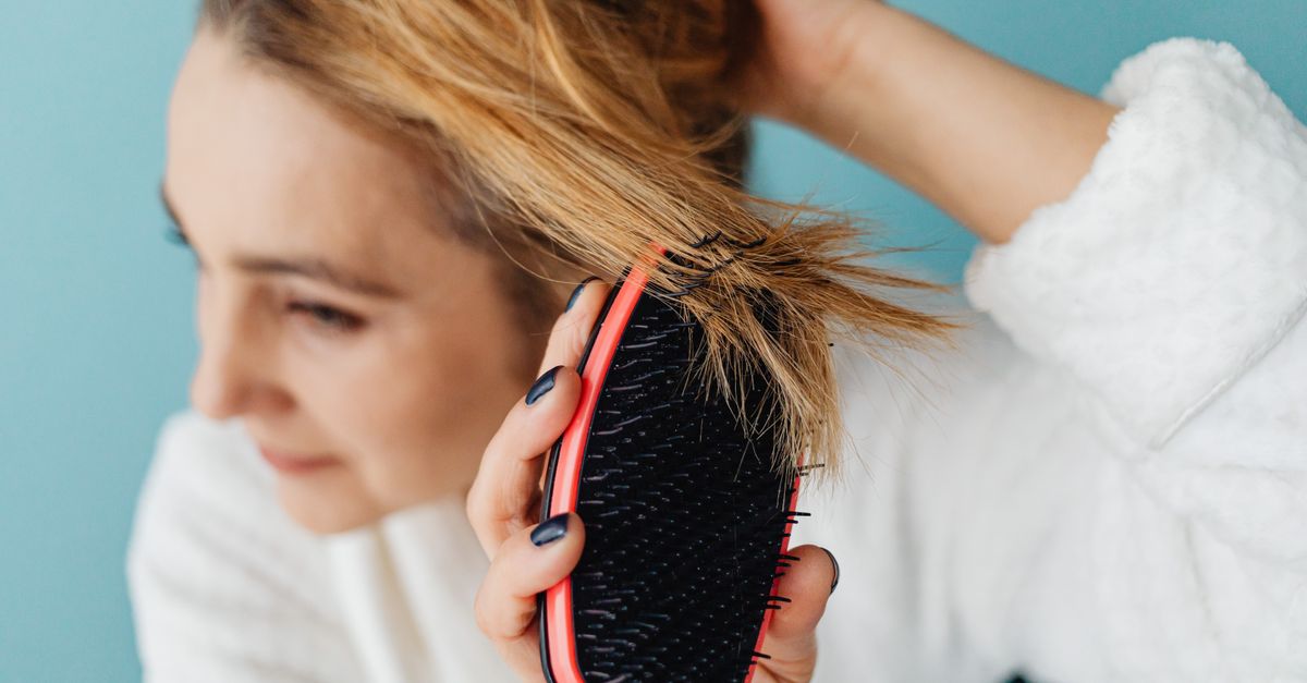 Close-up of a woman brushing her blonde hair with a red hairbrush indoors.