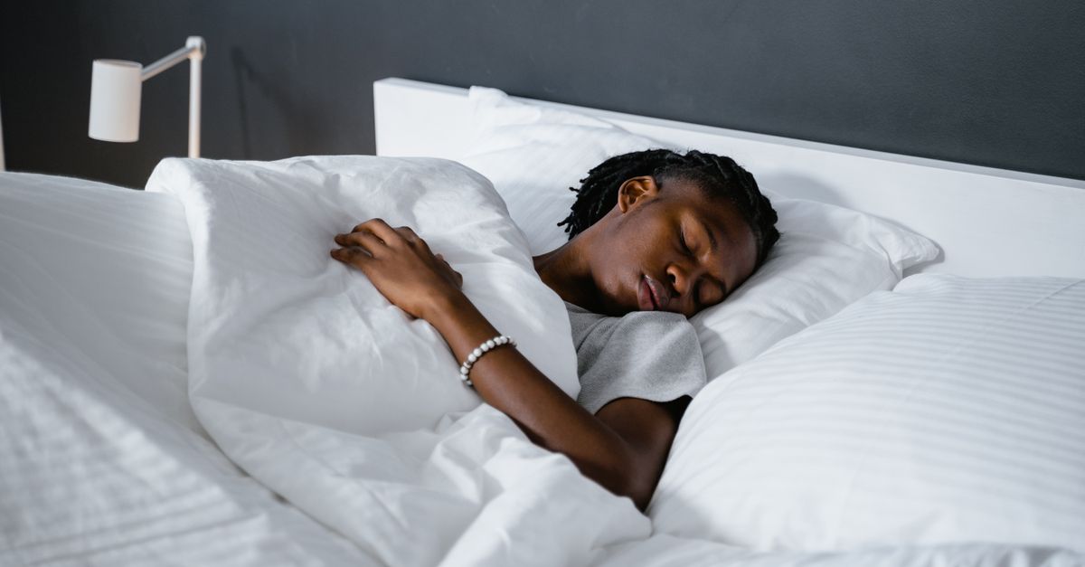 A man sleeping peacefully under a white blanket in a cozy bedroom.