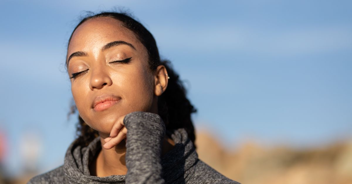 Close-up of a serene woman with eyes closed, enjoying sunlight outdoors. Soft focus background.