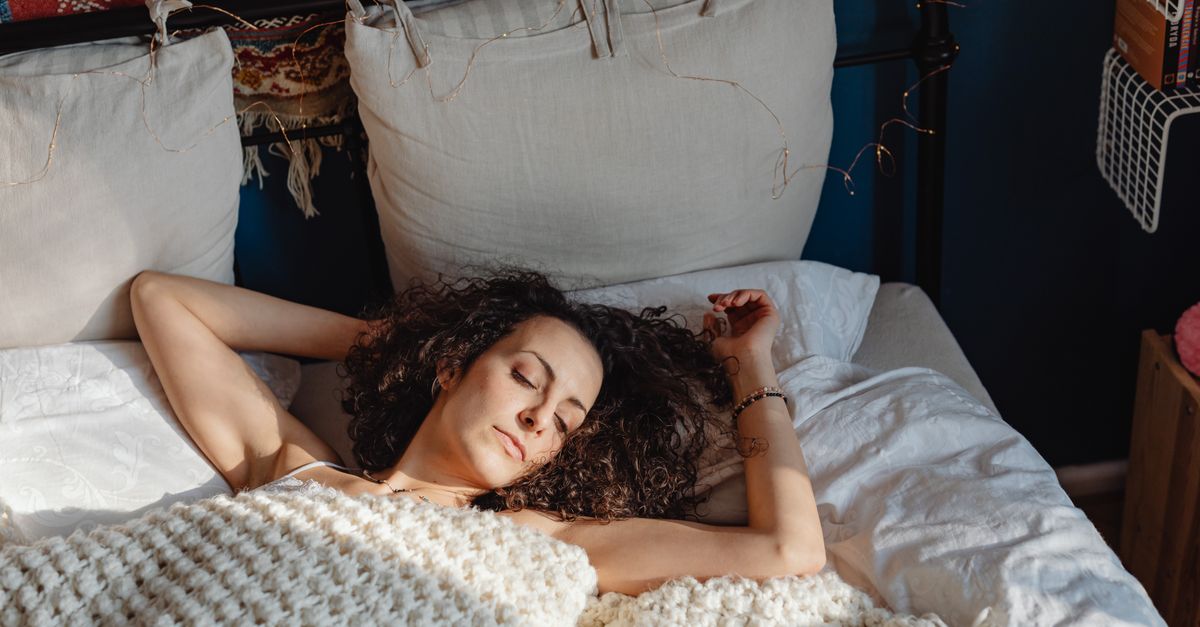 A woman enjoying a peaceful slumber in a cozy, sunlit bedroom with white linens.