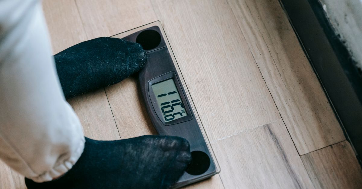 From above of unrecognizable person in socks standing on electronic weighing scales while checking weight on parquet during weight loss