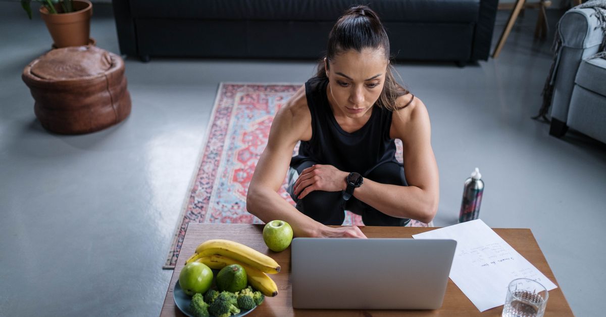 Woman using laptop at home with healthy fruits and vegetables on the table.