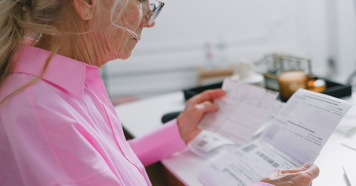 Elderly woman in a pink shirt reviewing paperwork at home.