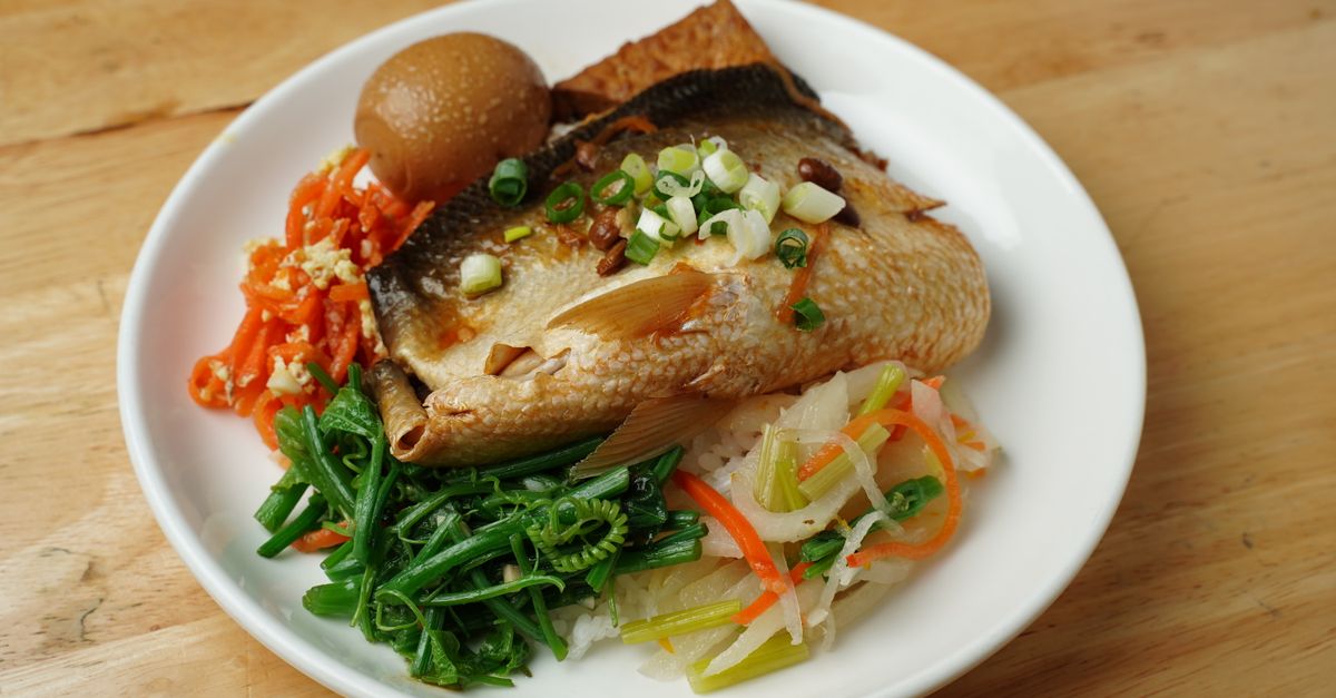A vibrant dish featuring fish, boiled egg, and fresh vegetables on a white plate.
