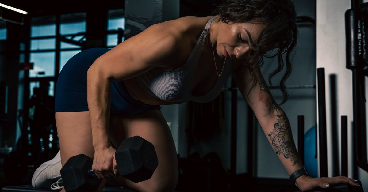 A woman performs a strength workout lifting a dumbbell in an indoor gym, demonstrating determination and fitness.