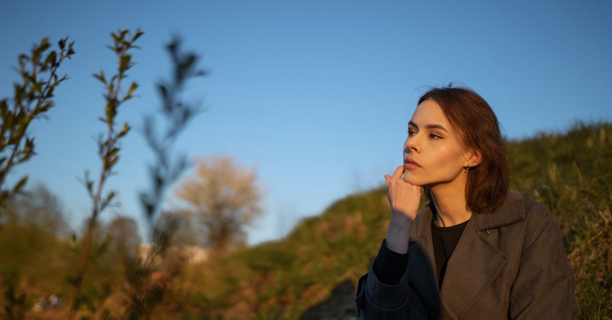 A thoughtful young woman sits outdoors, enjoying the sunlight and contemplating nature.