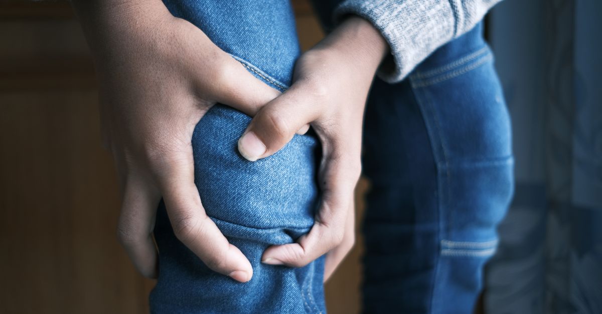 Close-up image of hands holding a knee in jeans, indicating pain or injury.