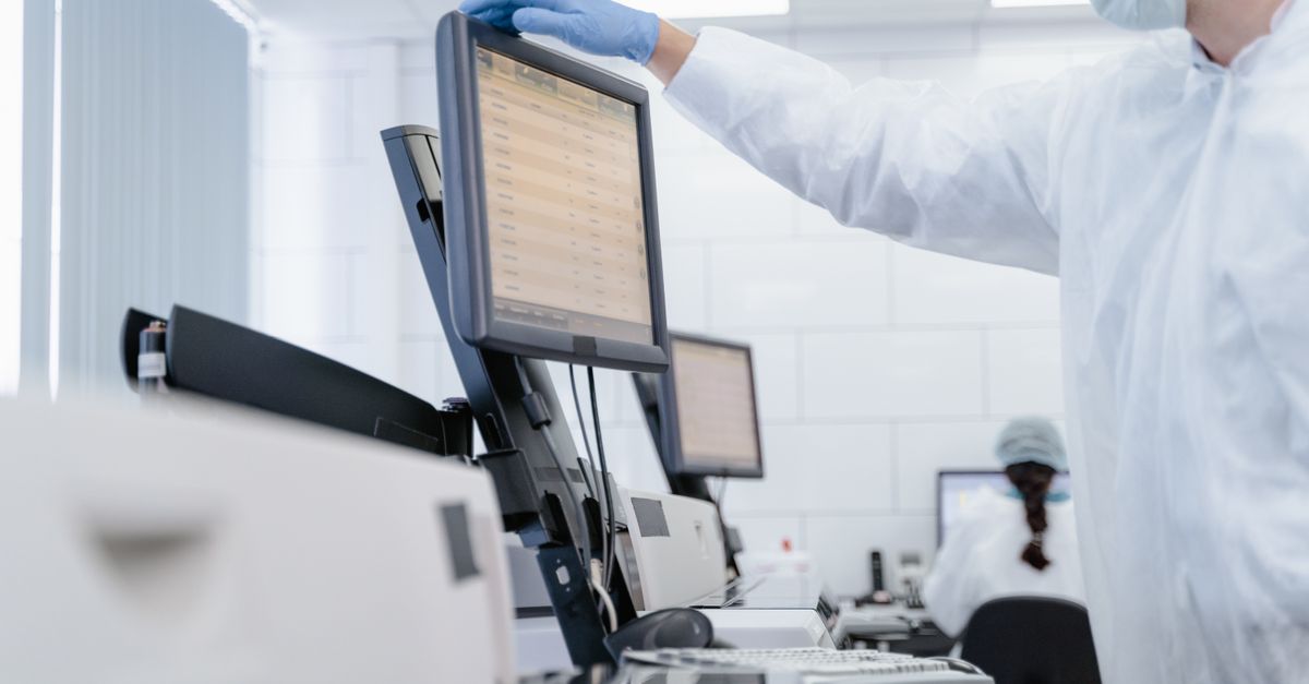 Researcher in PPE reviews data on a digital screen in a modern laboratory setting.