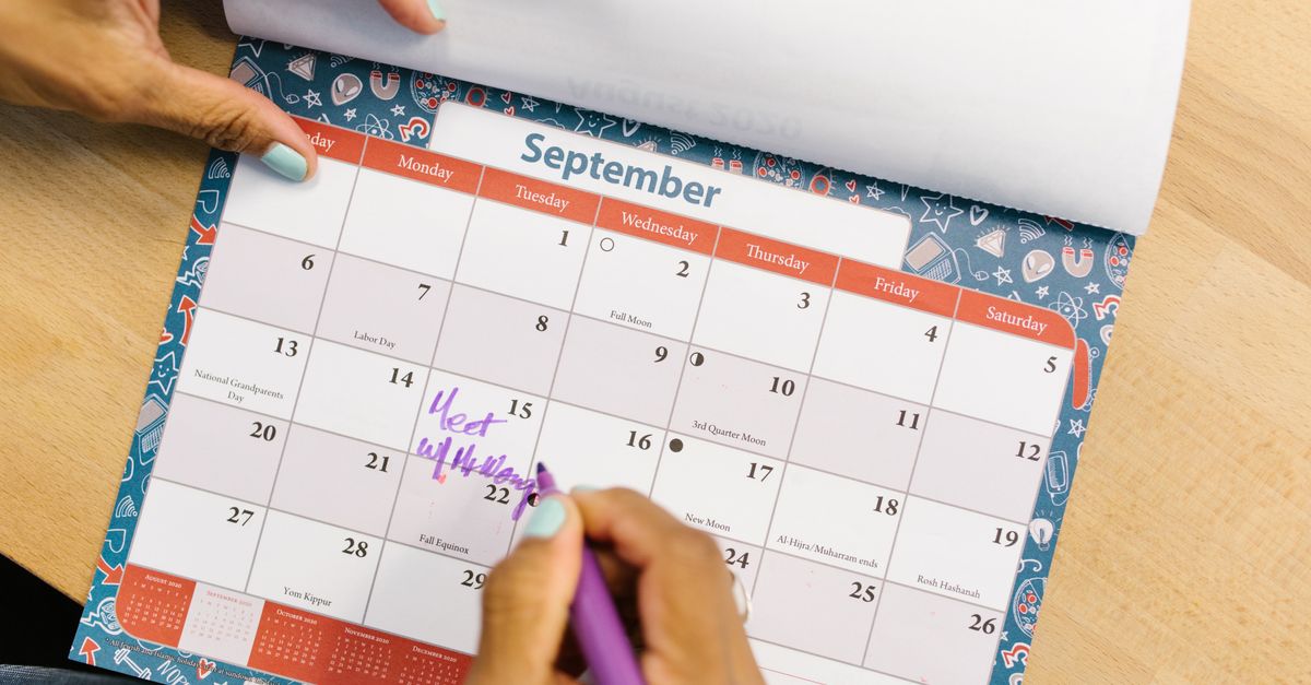 A person marking a calendar in September with a purple pen on a wooden desk.