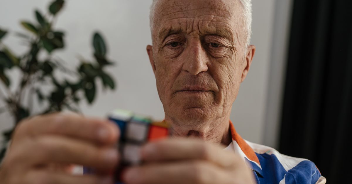 Elderly man concentrating on solving a Rubik's Cube, showcasing focus and mental agility.