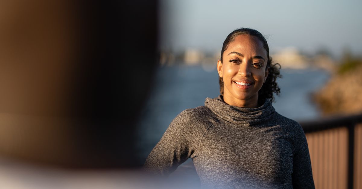 A confident woman smiling while enjoying a sunny day outdoors in a turtleneck sweater.