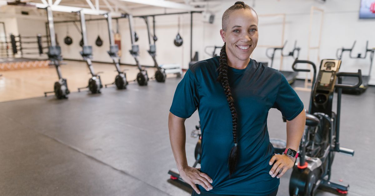 Smiling woman with braided hair standing confidently in a modern gym environment.