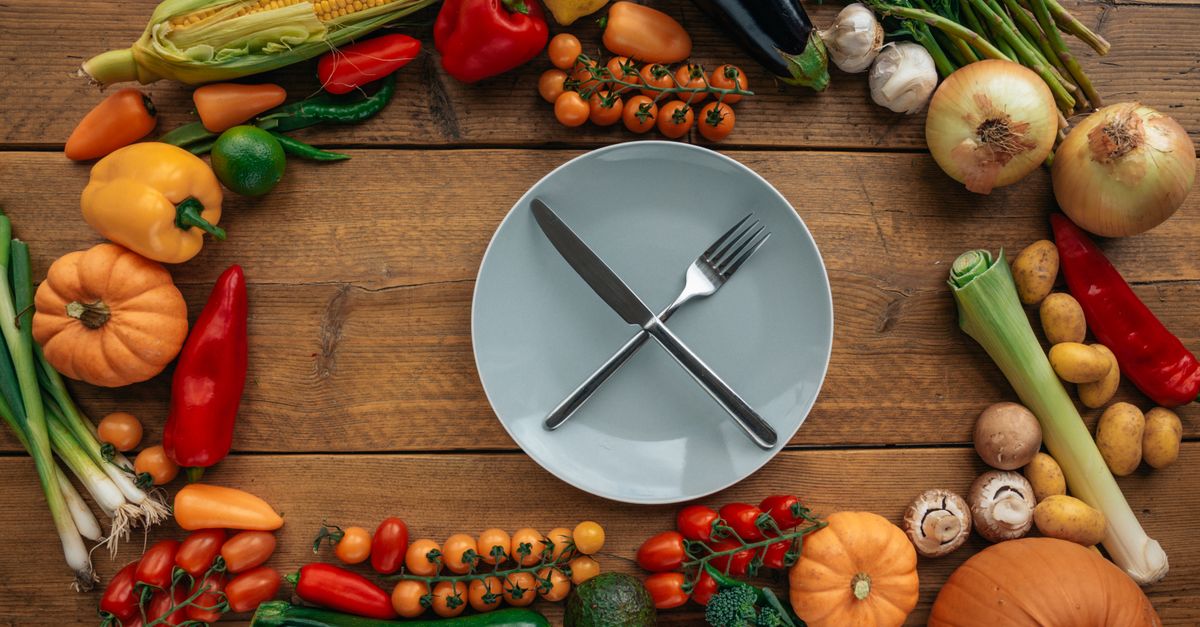 Top view of fresh vegetables creatively arranged around an empty plate on a wooden table.
