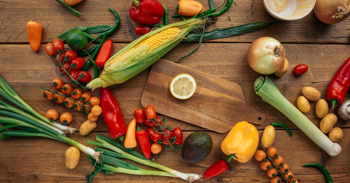 Colorful assortment of fresh vegetables and fruits arranged on a wooden table with cutting board.