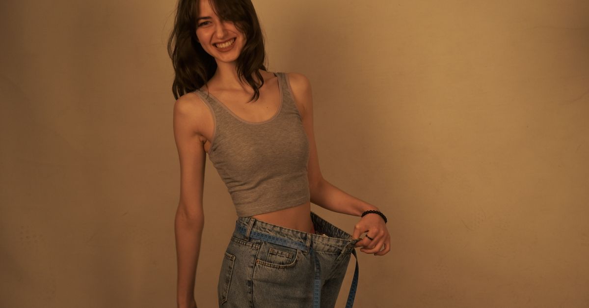 Joyful woman shows success in weight loss by wearing loose jeans. Healthy lifestyle concept.