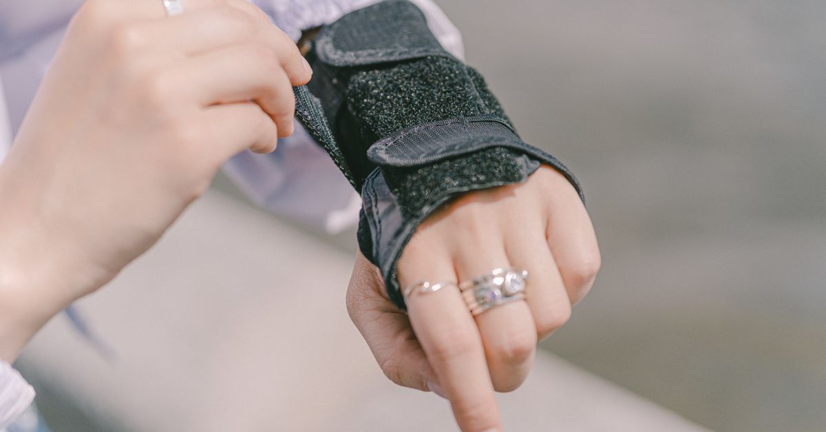 Detailed shot of a hand with rings adjusting a wrist brace, showcasing protection and style outdoors.