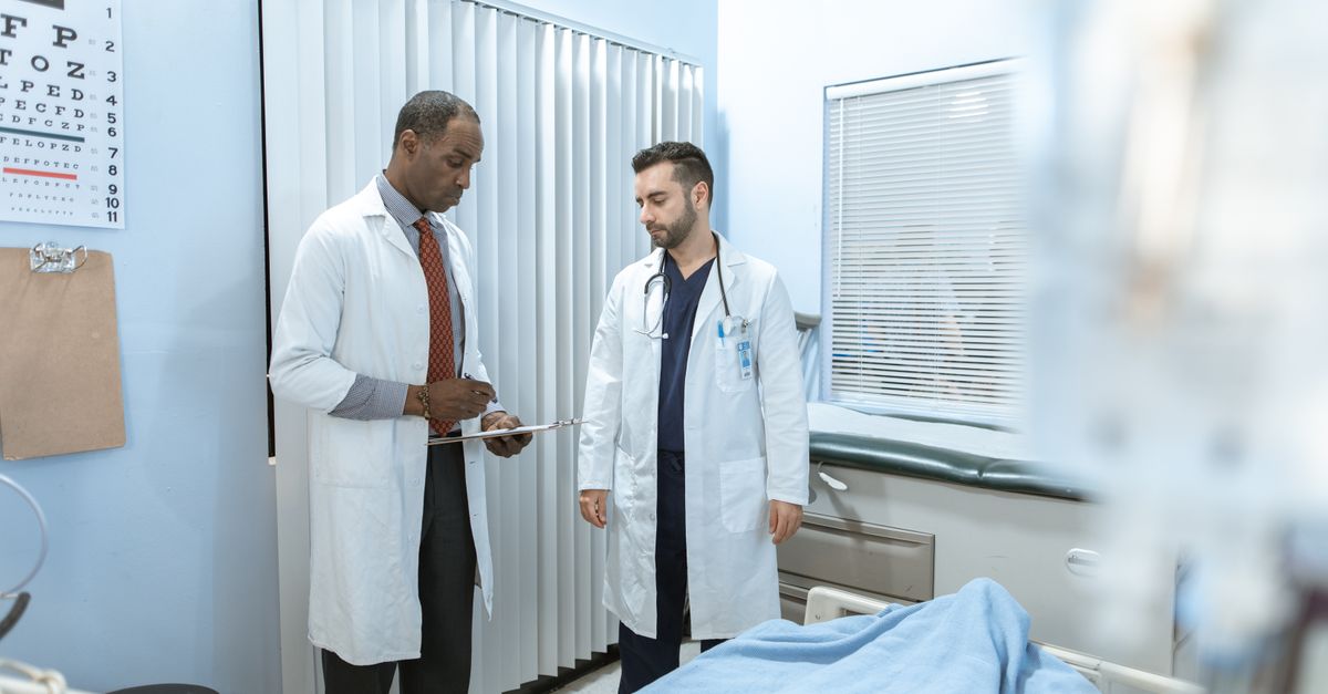 Two doctors review a patient's chart in a hospital room, focusing on healthcare cooperation and medical care.