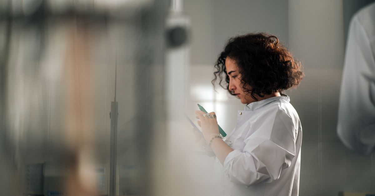 A focused female scientist with curly hair writes notes in a laboratory setting.