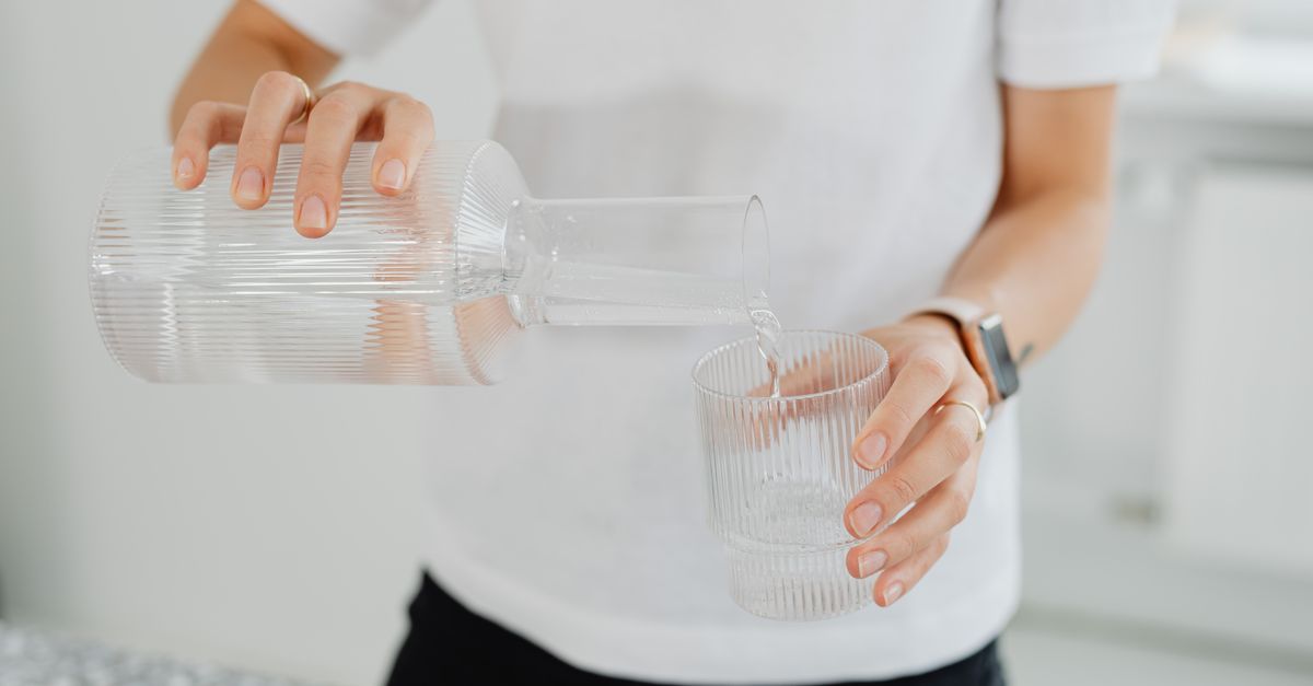 A person pouring water from a carafe into a glass on a countertop indoors.