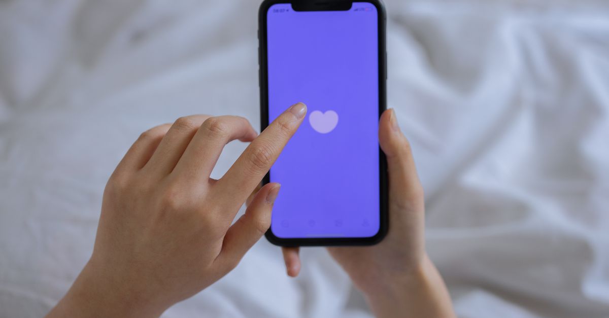 Close-up of hands using a smartphone with a heart icon on screen, representing technology and connection.