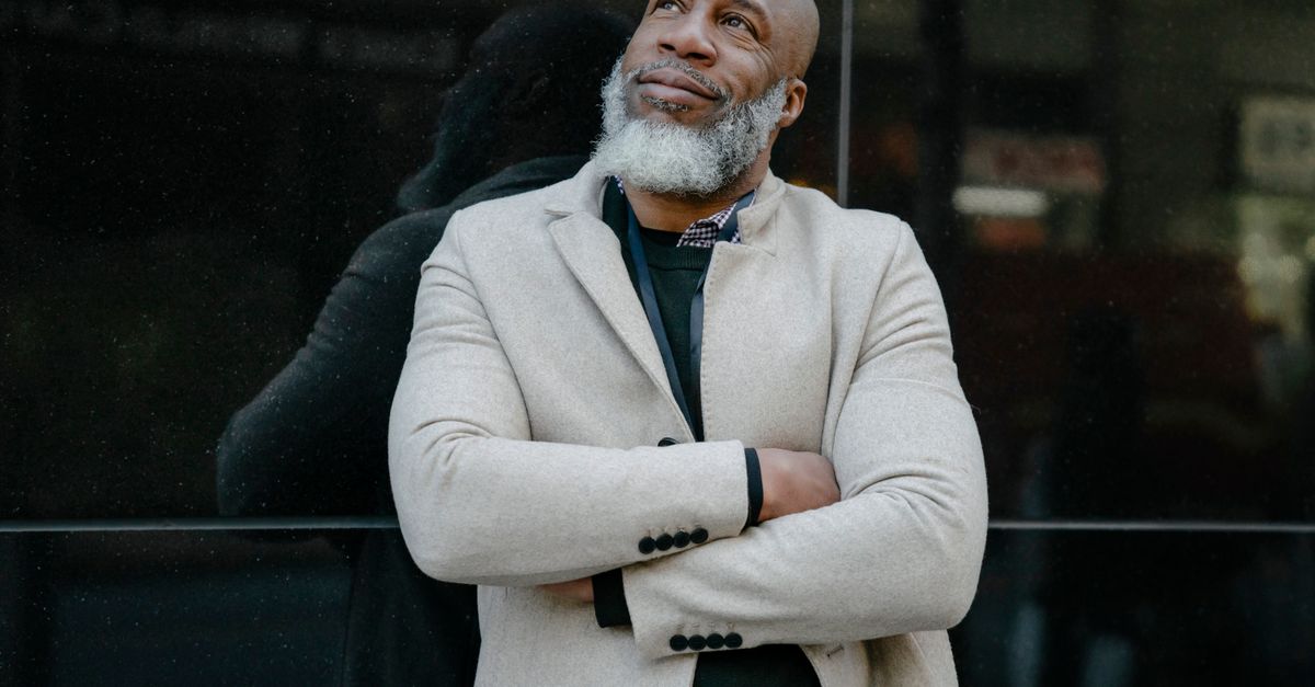 Mature man smiling confidently while leaning against a reflective surface in an urban setting.