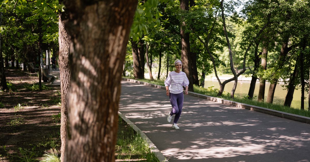 A senior woman jogging along a tree-lined path on a sunny day, embracing a healthy lifestyle.