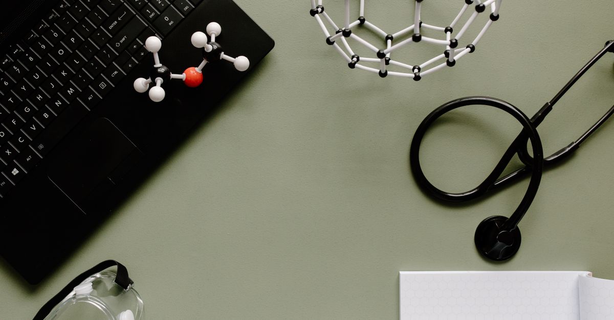 Medical workspace with laptop, molecules, and stethoscope on green background.