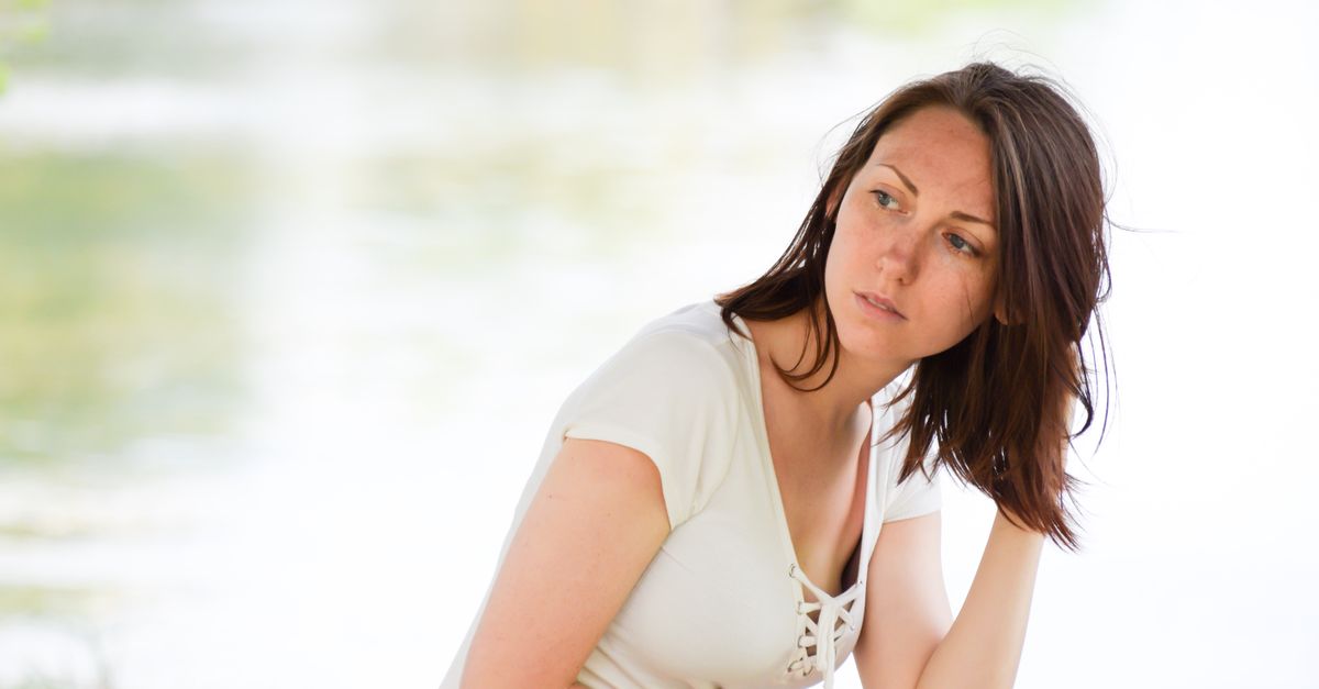 Young woman gazing thoughtfully by a serene lake, capturing a moment of calm reflection.